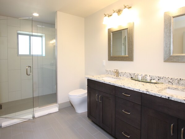 A modern bathroom with a glass shower enclosure, a white toilet, dark wooden cabinets, and a marble countertop.