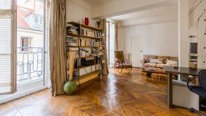 A spacious living room with a wooden parquet floor, a bookshelf, a green exercise ball, a sofa, and a dining table. - Classic Style by Rue Montorgueil, by Veeve (Paris)