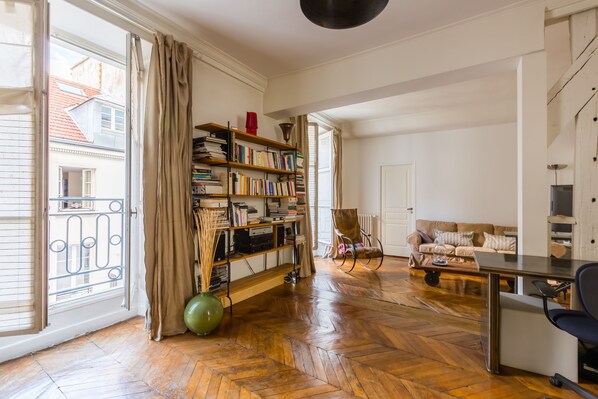 A spacious living room with a wooden parquet floor, a bookshelf, a green exercise ball, a sofa, and a dining table.