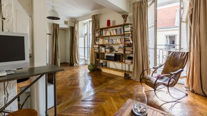 A spacious living room with a wooden herringbone floor, a bookshelf filled with books, a comfortable armchair, and a television on a wooden table. - Classic Style by Rue Montorgueil, by Veeve (Paris)