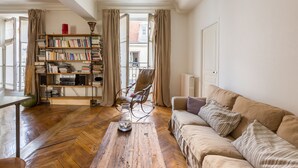 A cozy living room with a wooden herringbone floor, a beige sofa, a bookshelf, and a chair. - Classic Style by Rue Montorgueil, by Veeve (Paris)