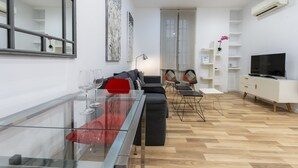 A modern living room with a glass dining table, red chairs, a grey sofa, and a TV on a white cabinet. - Modern Madrid Downtown Puerta Del Sol M (PRE2B) (Madrid)