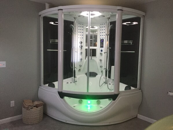 Un espace de spa moderne et fermé, doté d’une paroi en verre, d’un panneau de commande et d’un sol éclairé en vert.