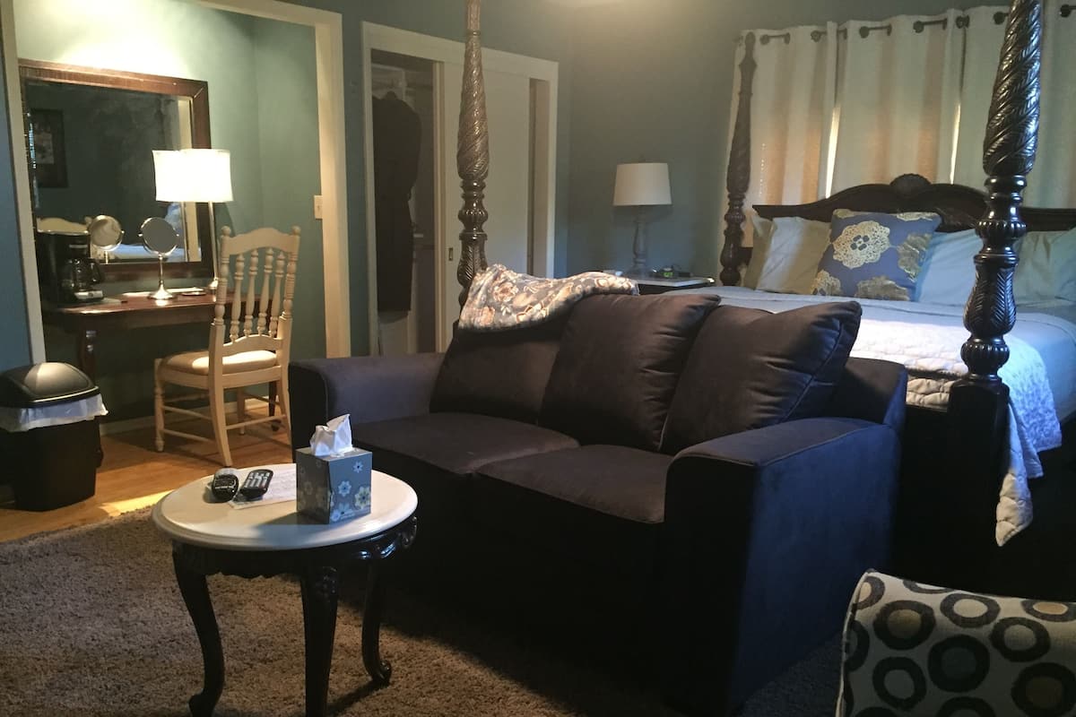 A bedroom with a four-poster bed, a sofa, a small table with a tissue box, a chair, and a lamp.