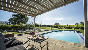 A poolside area with a pergola, lounge chairs, and a table with drinks and flowers. - CHARMING VILLA IN THE HEART OF CHIANTI (terranuova bracciolini)