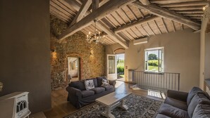 A spacious living room with a stone wall, a wooden ceiling, and a large window. - CHARMING VILLA IN THE HEART OF CHIANTI (terranuova bracciolini)