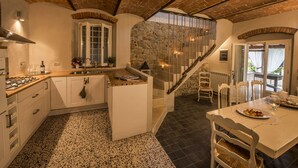 A kitchen with a central island, white cabinetry, and a stone wall. There is a staircase leading to a balcony with outdoor seating. - CHARMING VILLA IN THE HEART OF CHIANTI (terranuova bracciolini)