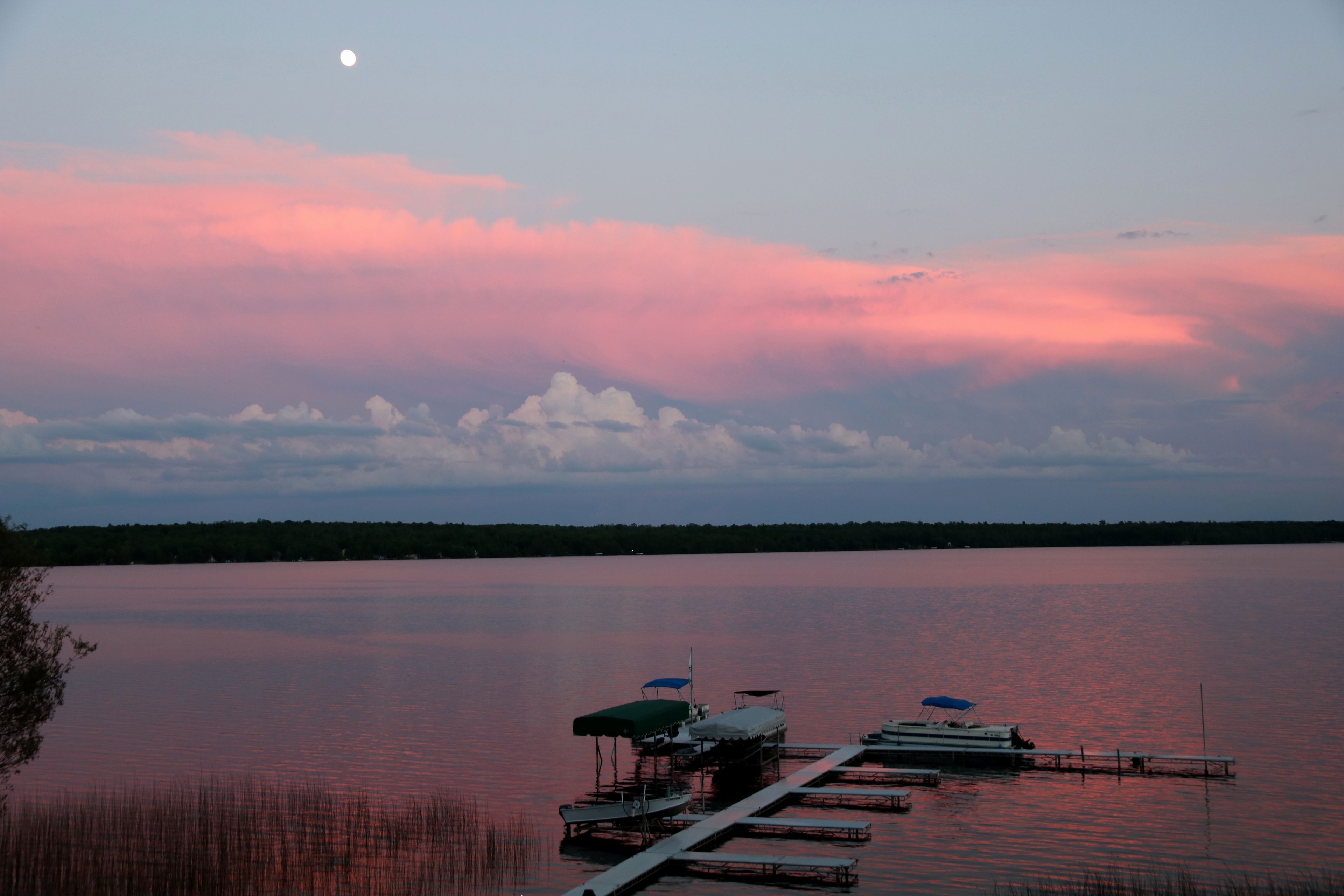 A calm lake at dusk with a dock extending into the water, surrounded by trees.