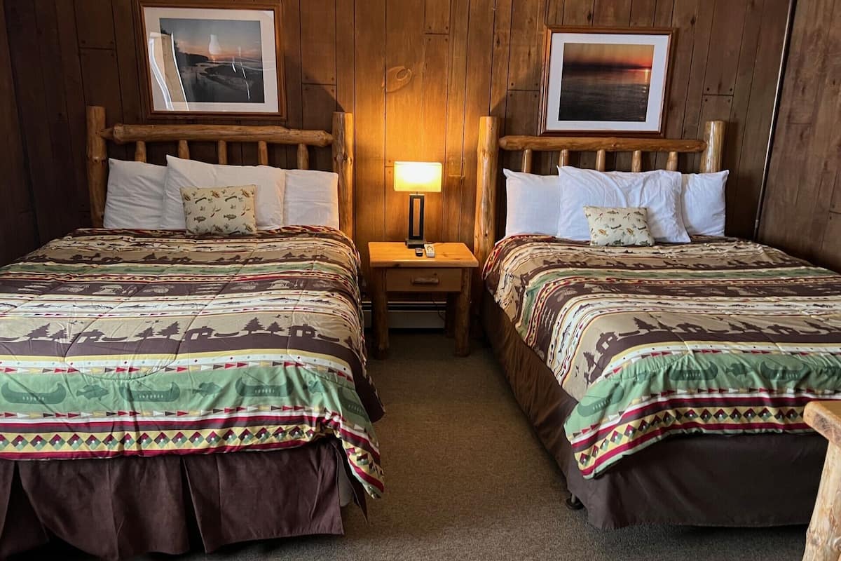 Une chambre avec deux lits en bois, chacun doté d’une tête de lit, d’une table de chevet, d’une lampe et de tableaux encadrés accrochés aux murs.