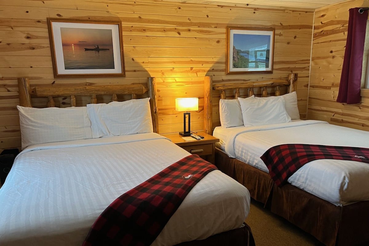 Une chambre avec deux lits, des murs en bois et des tableaux encadrés.