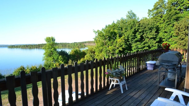 A wooden deck with a view of a lake, a barbecue grill, and outdoor seating. - AJ's Lodge and Oven (Bergland)