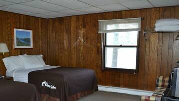 Una habitación de hotel con paneles de madera, una cama, un escritorio, una silla, un ventanal con persianas y una cafetera.