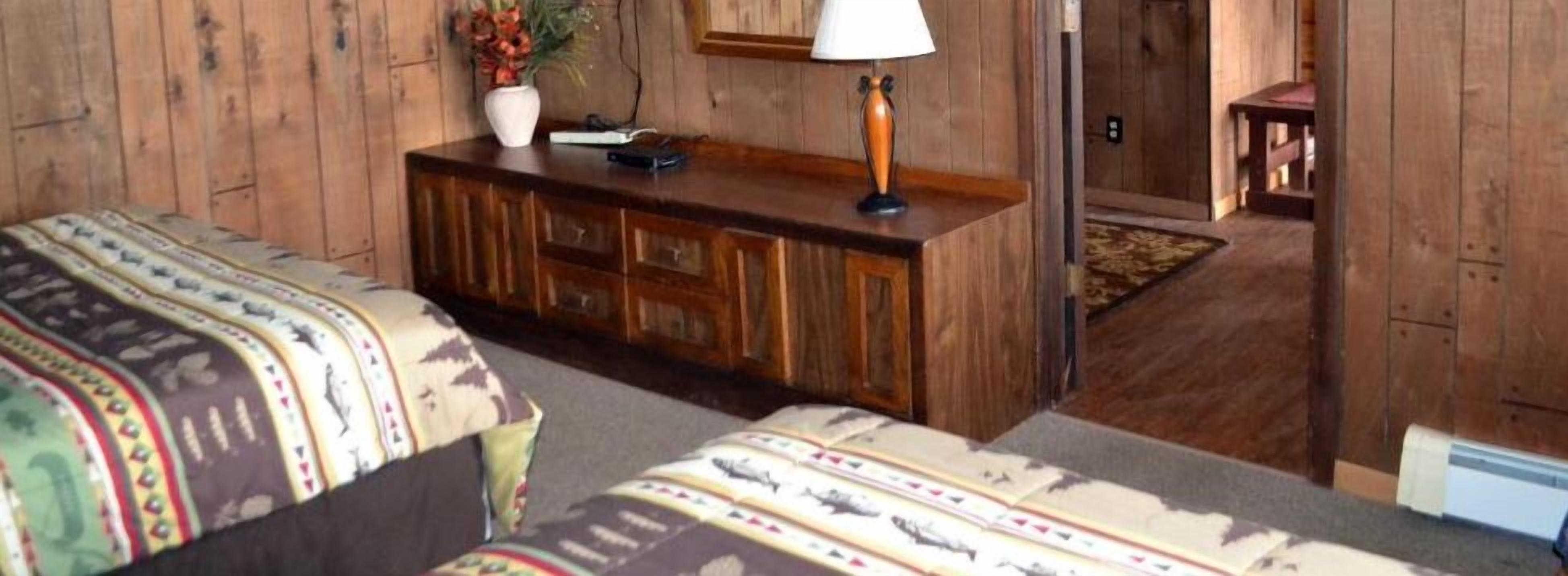 A room with a wooden bed, a wooden dresser, and a lamp.