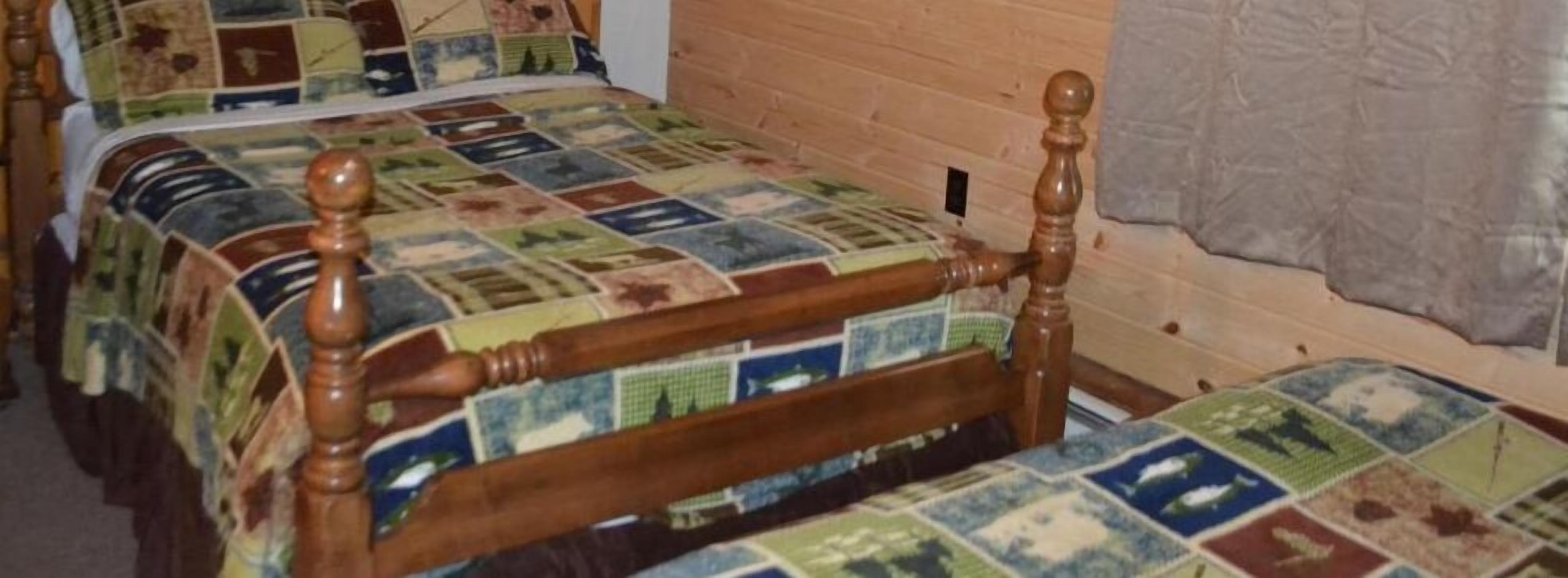 Una stanza con due letti in legno, complete di poggiatesta, una parete in legno e una coperta trapuntata.