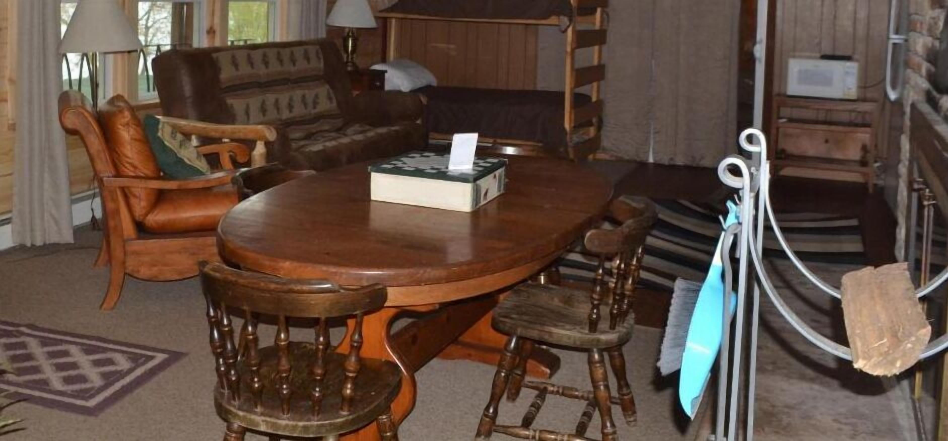 A cozy living room with a wooden table, leather armchairs, and a sofa.