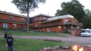 A lodge with a wooden exterior, a deck, and a fire pit in the foreground. - AJ's Lodge and Oven (Bergland)