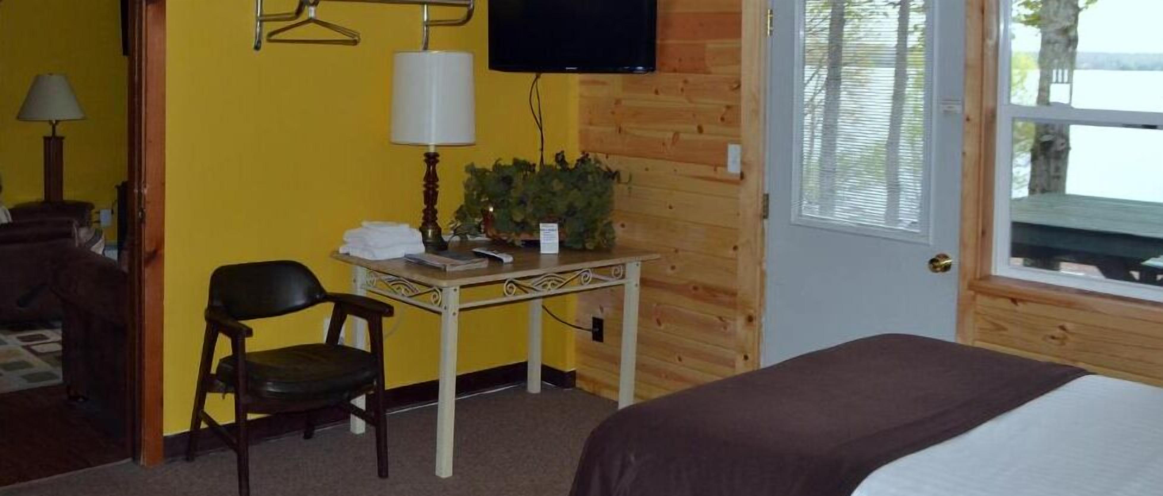 A hotel room with a bed, a desk with a lamp, a chair, a television, and a window with blinds.