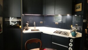 Una cocina moderna con armarios oscuros, encimera blanca, estufa a gas, cafetera y un jarrón con una flor rosa.