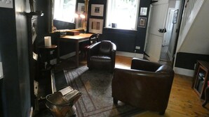 Una habitación con pared oscura, un escritorio de madera, un sillón de cuero, un espejo y una ventana.