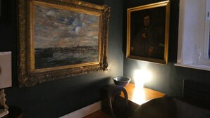 Una habitación con una pared oscura, una mesa de comedor de madera y dos cuadros enmarcados.