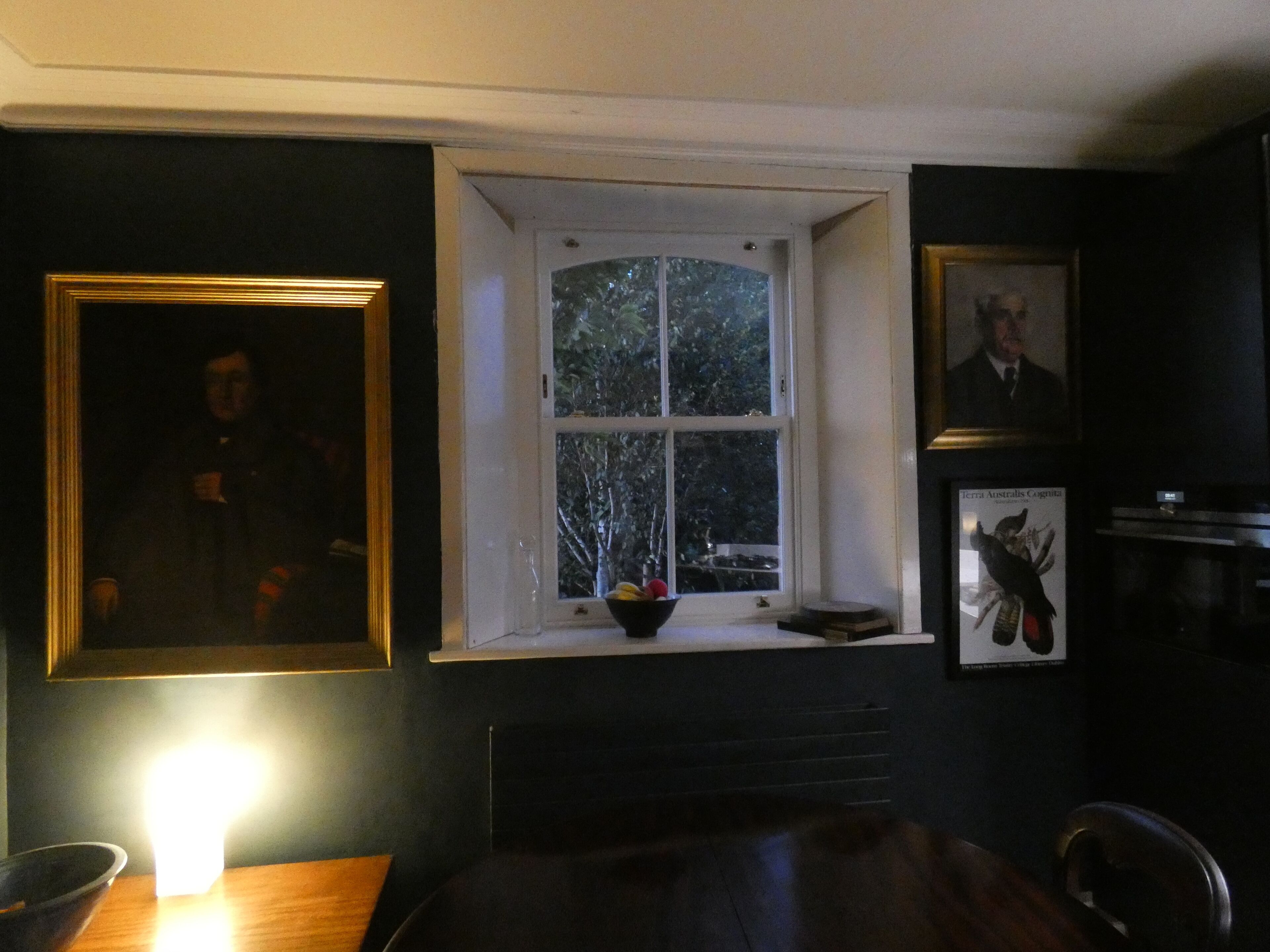 A room with a window, a framed picture, a table, and a chair.