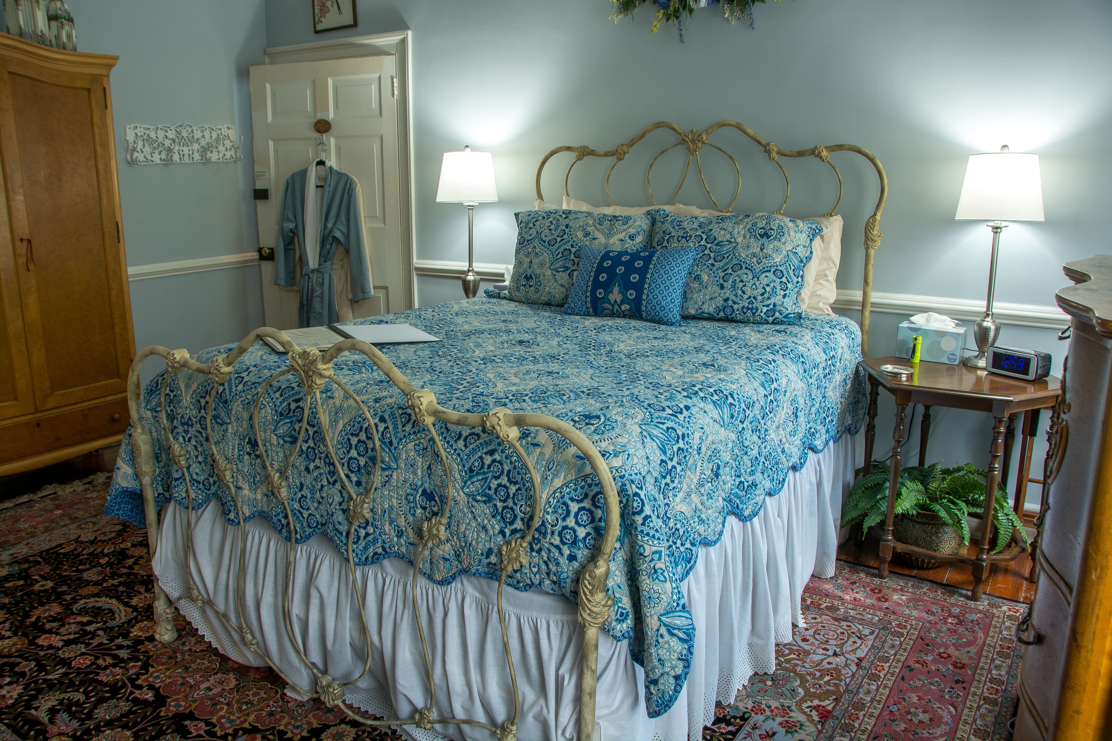 A bedroom with a bed, two bedside lamps, a wooden wardrobe, a door, and a patterned rug.