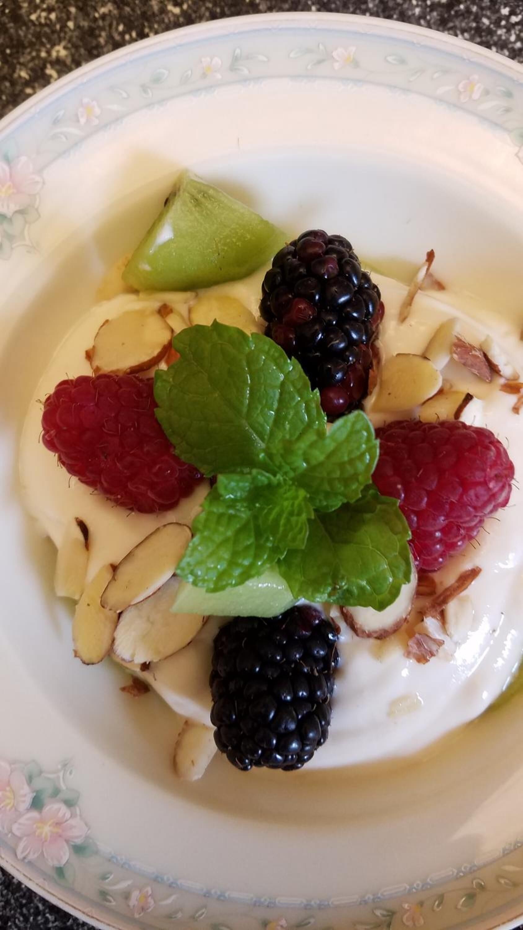 A bowl of yogurt topped with blackberries, raspberries, mint leaves, and sliced almonds.
