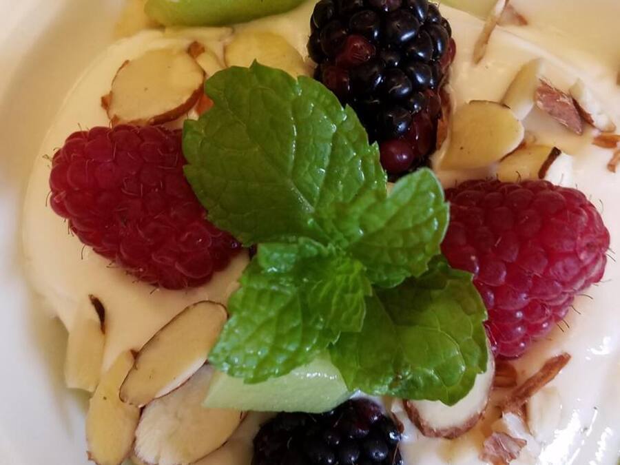 A bowl of yogurt topped with blackberries, raspberries, mint leaves, and sliced almonds.
