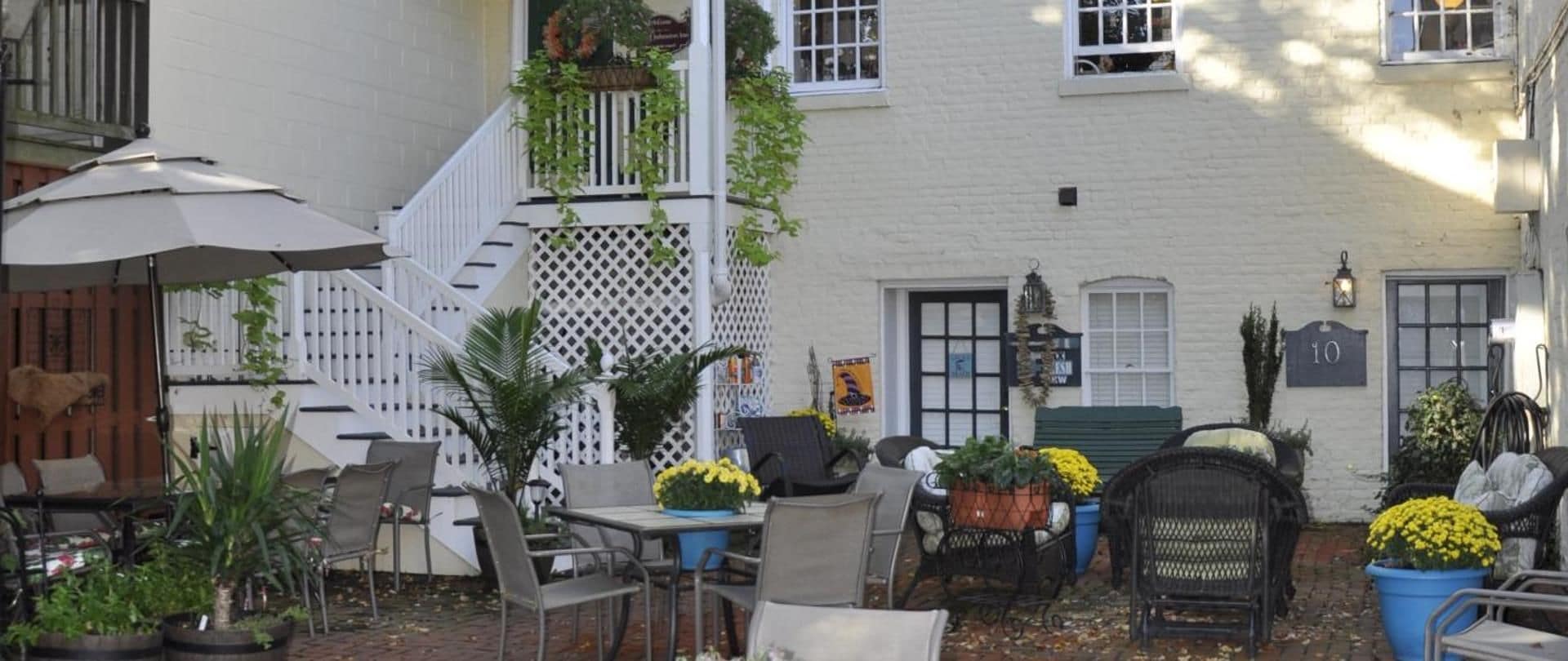 A courtyard with outdoor seating, potted plants, and a white building with a sign.