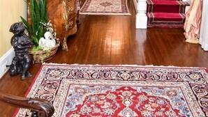Un amplio vestíbulo con alfombra roja, candelabro, escalera y un espejo grande.