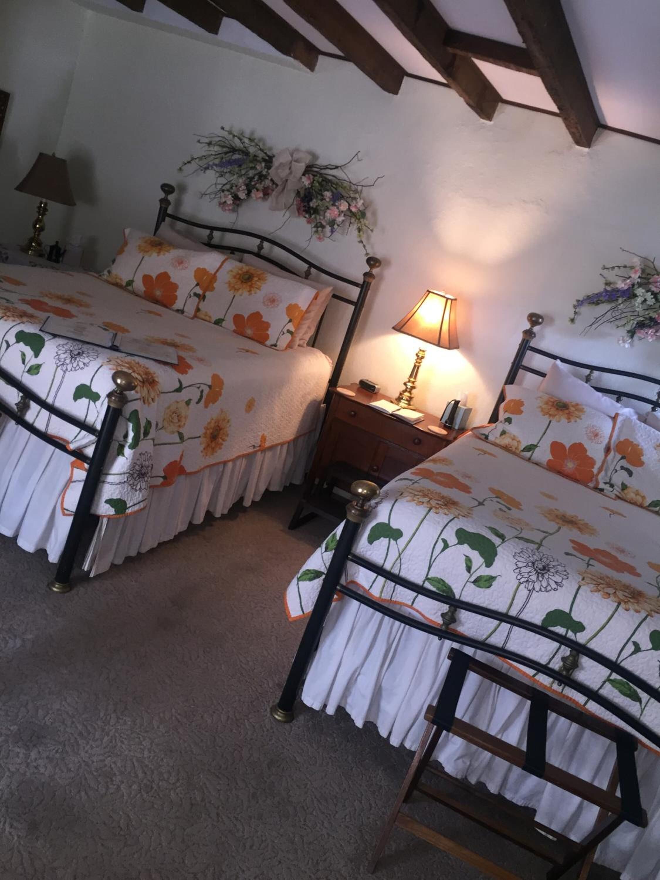Habitación con dos camas, cada una con una colcha estampada y almohadas a juego. Entre las camas, una mesita de noche con una lámpara.