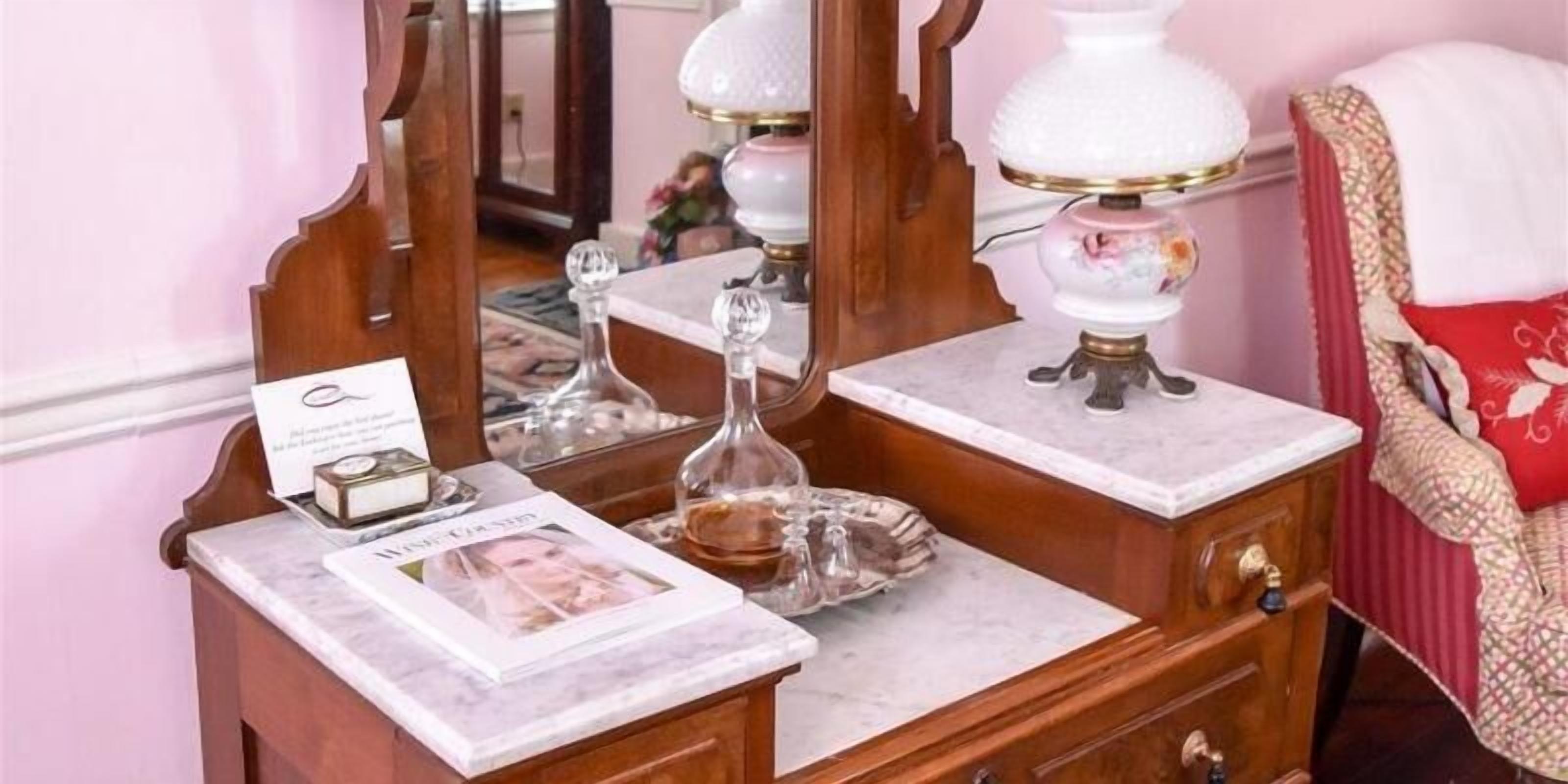 Un tocador de madera con encimera de mármol, un espejo, una lámpara y una fotografía enmarco.