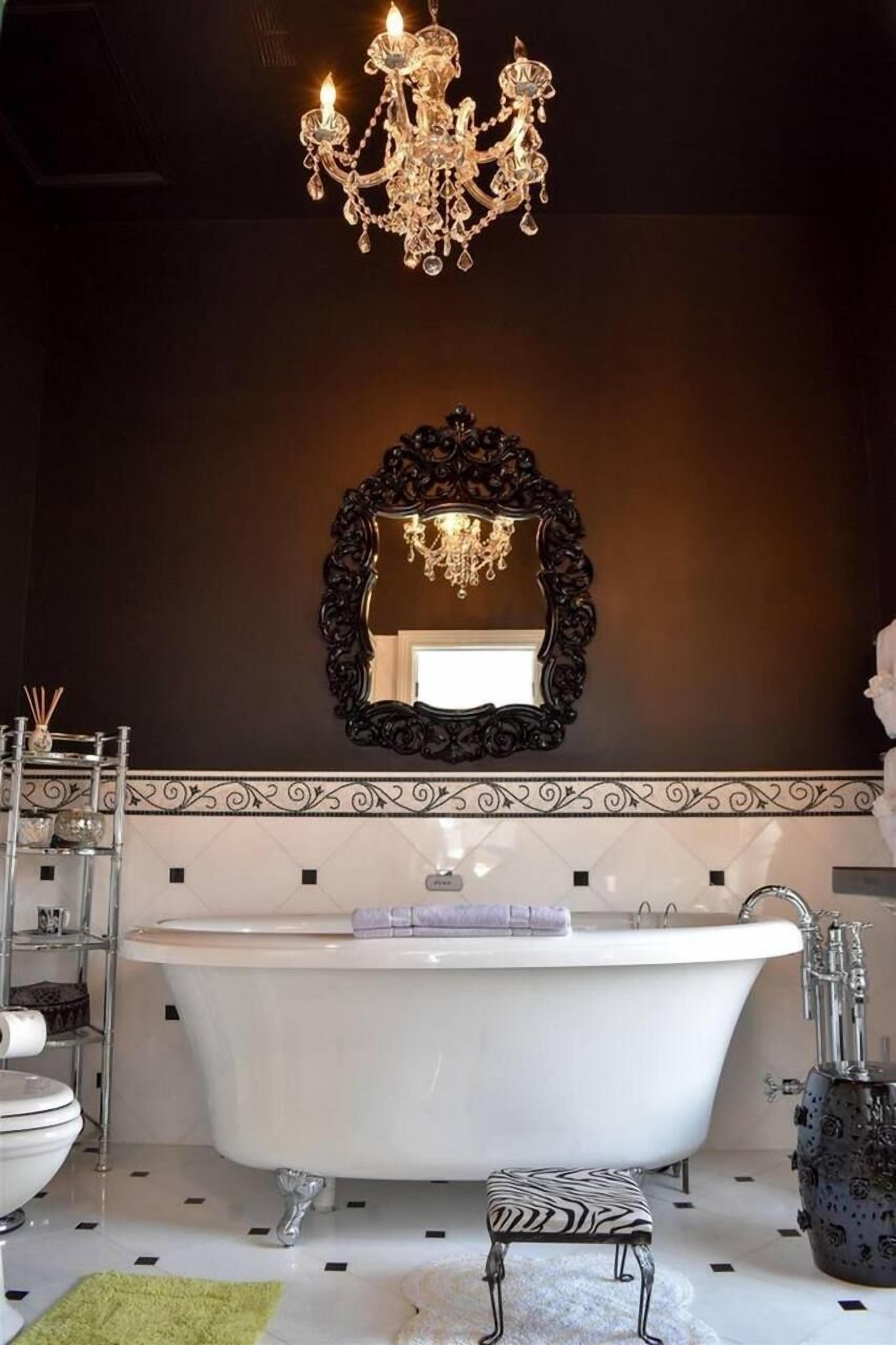 A bathroom with a freestanding bathtub, a large ornate mirror, and a chandelier.