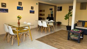 A spacious room with a glass-top dining table, white chairs, and a potted plant.