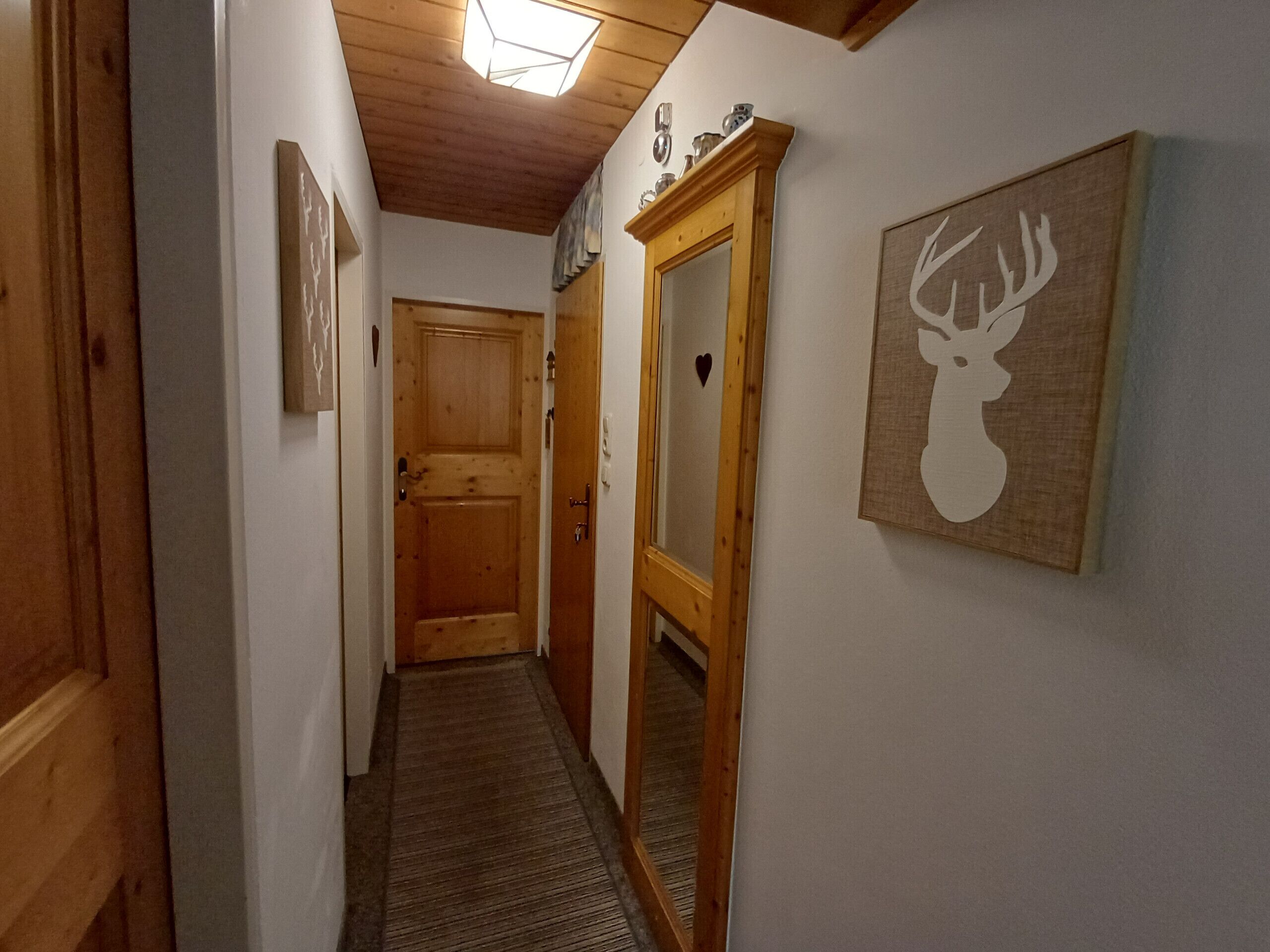 A hallway with wooden doors, a mirror, and a deer head artwork on the wall.