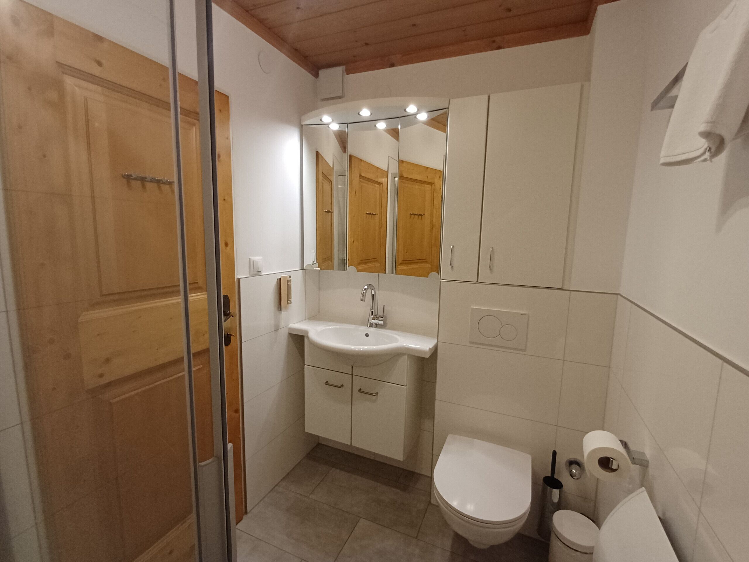 A bathroom with a wooden door, a white sink, a mirror, and a toilet.