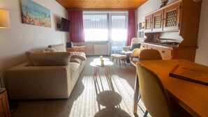 Ein gemütliches Wohnzimmer mit einer Couch, einem Esstisch und einer Küchenzeile mit Schränken.
