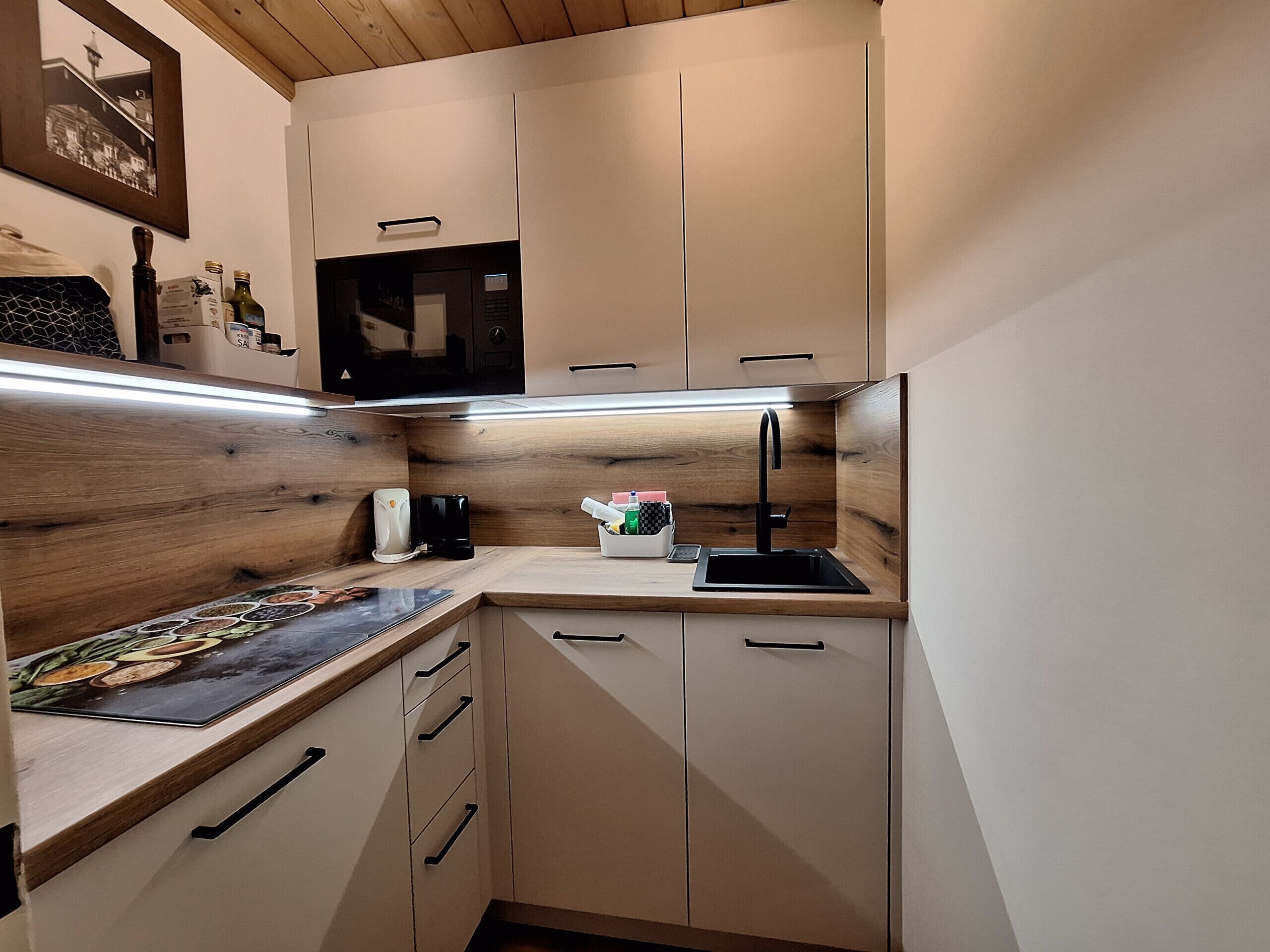 A compact kitchen with wooden cabinetry, a microwave, a sink, and a countertop with various items.