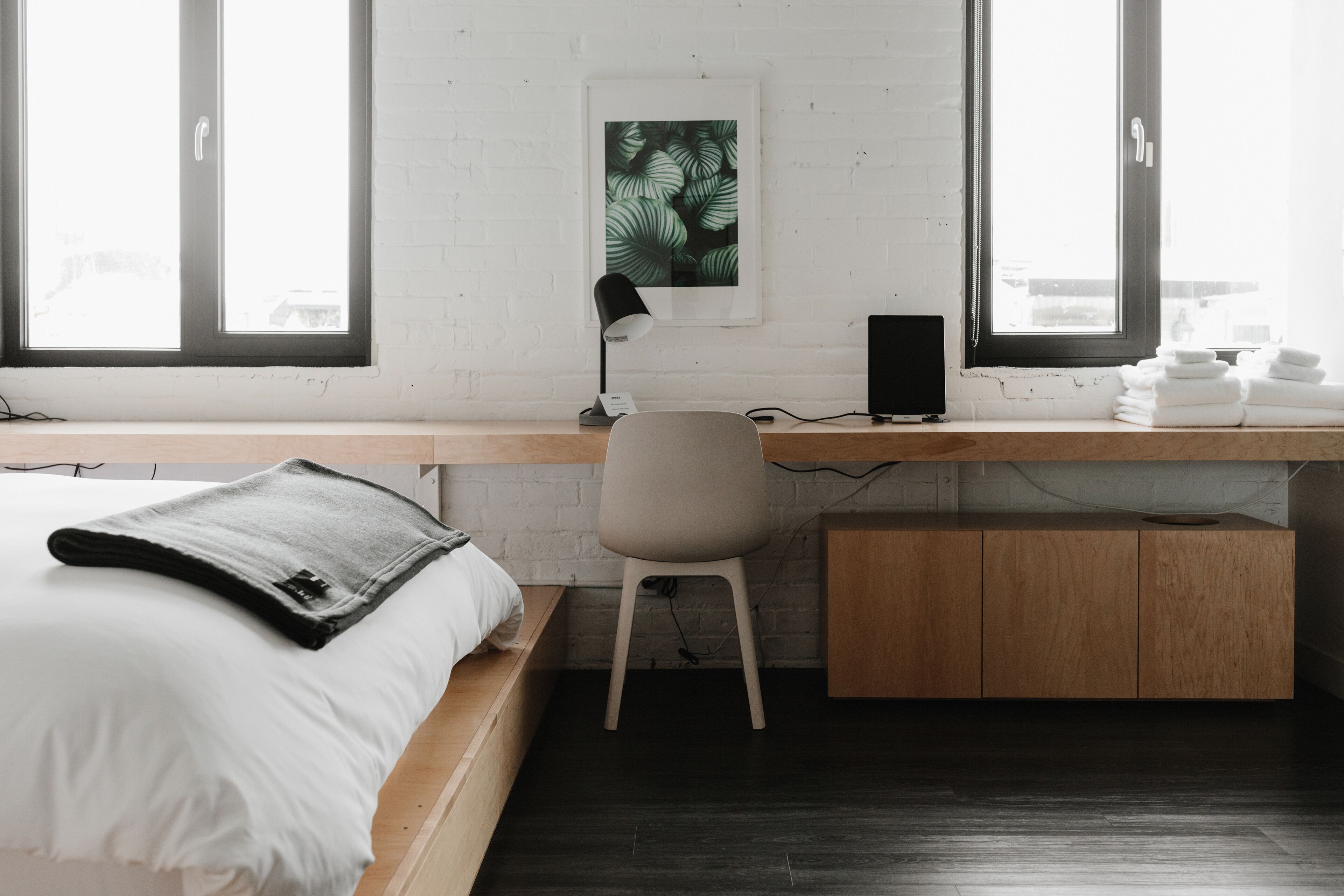 A modern bedroom with a bed, desk, chair, and a view of the city through large windows.