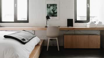 A modern bedroom with a bed, desk, chair, and a view of the city through large windows.