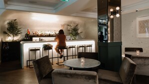 Een bar met een toog, barstoelen en een zithoek met ronde tafels en stoelen.