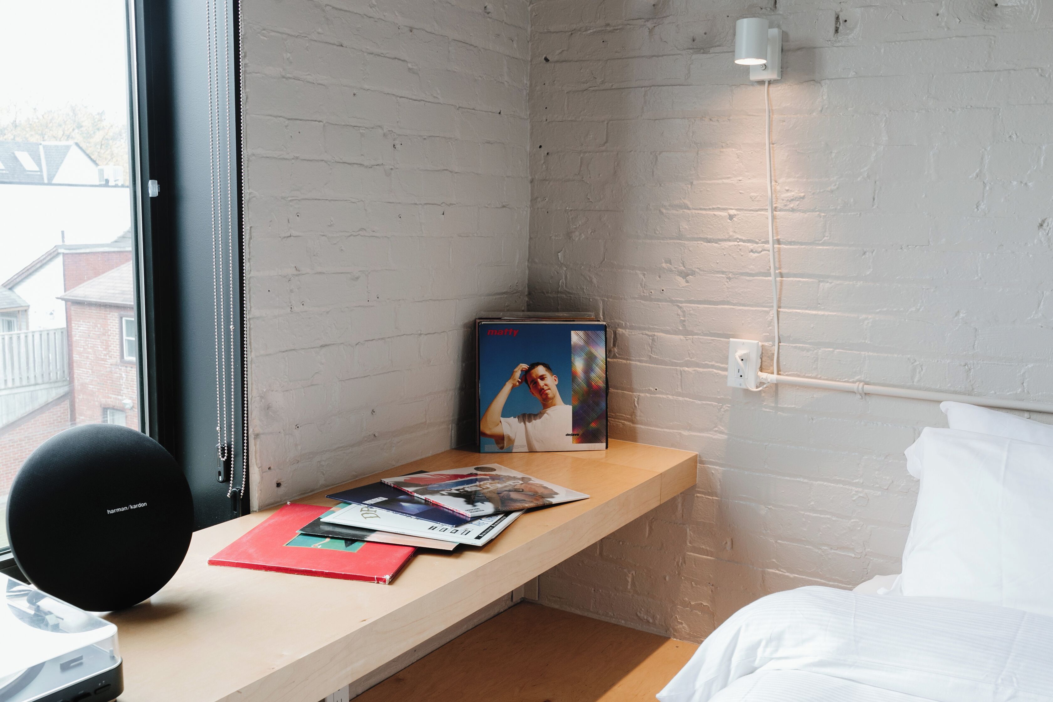 A room with a wooden desk, a black speaker, a framed photo, and a bed with white bedding.