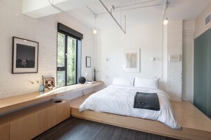 Een moderne slaapkamer met een ingebouwde bank, grote ramen en kunst aan de muur.