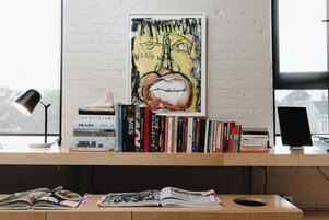A bookshelf with various books, a framed artwork, and a desk lamp.