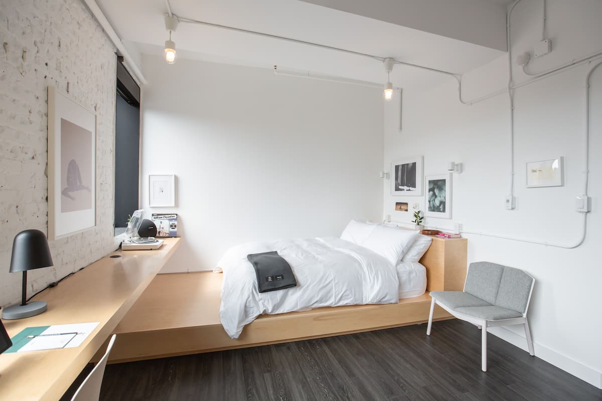 Een minimalistische slaapkamer met een bed, nachtkastje, stoel en kunstwerken aan de wanden.
