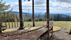 A wooden boardwalk with a wooden bench and a signpost in a forested area with a view of distant mountains.