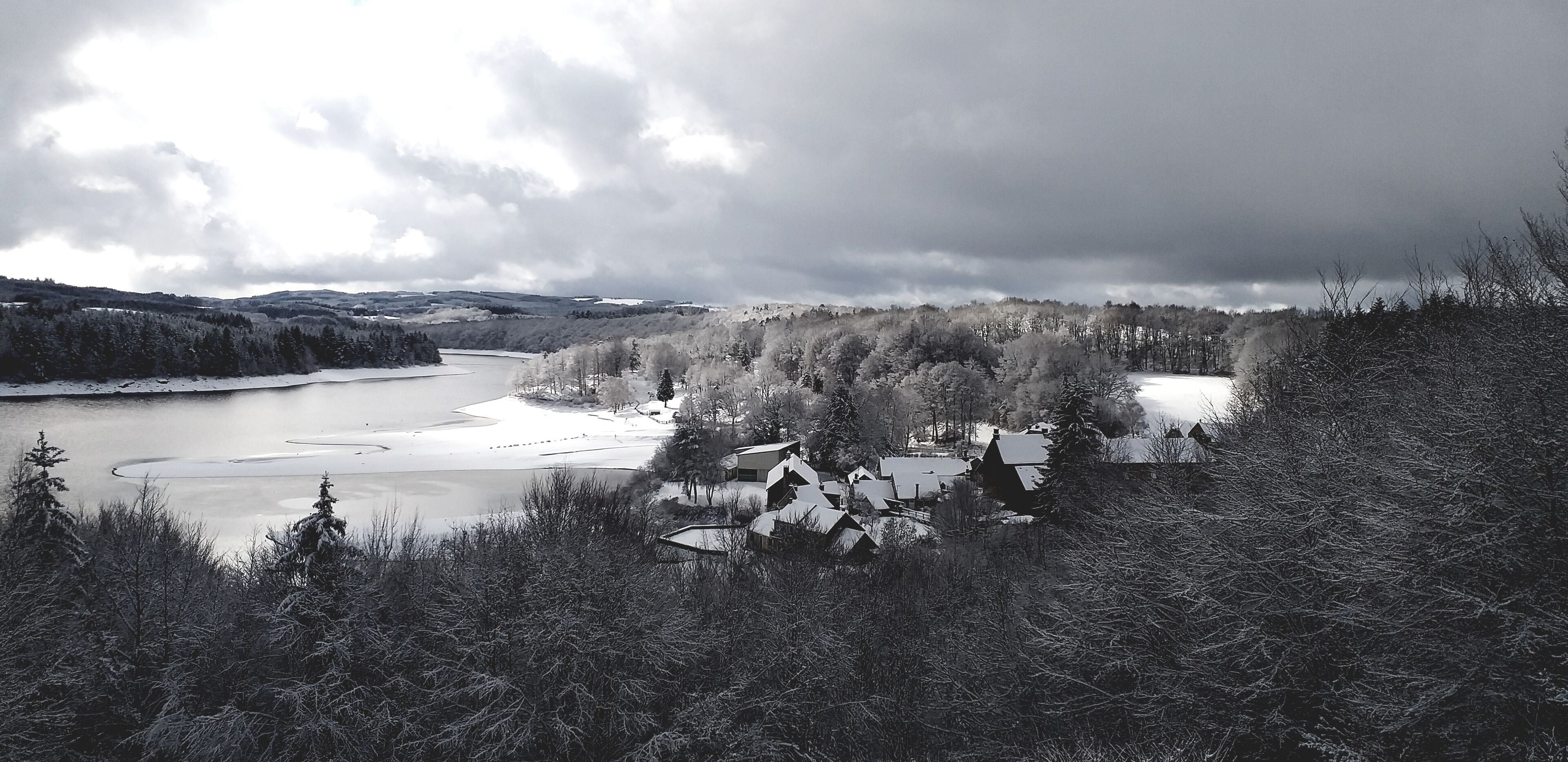 Un paysage hivernal avec une rivière, des arbres couverts de neige et des maisons aux toits inclinés.