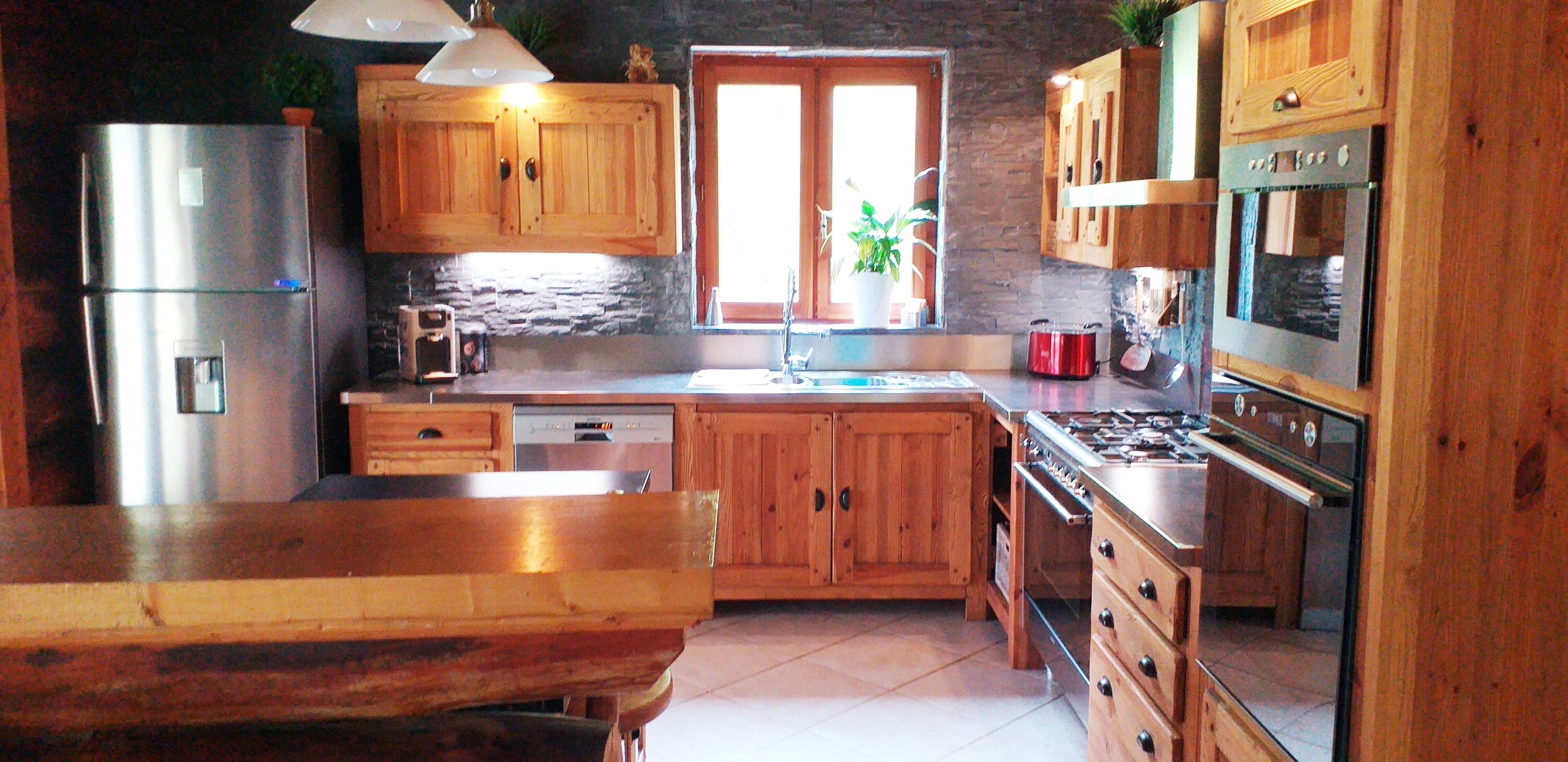 A kitchen with wooden cabinets, a stainless steel refrigerator, a dishwasher, a stove, and a window with a plant.