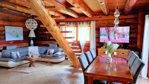 A log cabin interior with a wooden dining table, grey sofa, and a TV on the wall.