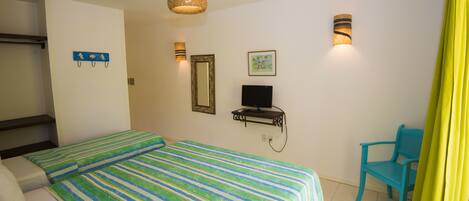 A hotel room with a bed, a desk with a computer, a chair, and wall-mounted lights.